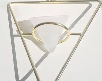 May include: A gold-colored metal geometric hanging planter with a triangular frame. A frosted glass cone-shaped vase is suspended within the frame. A delicate chain and ring are attached for hanging. The planter is designed for small plants or air plants.