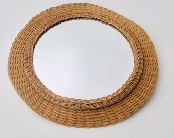 May include: A round woven wicker mirror with a natural brown color. The mirror has a simple design and is perfect for adding a touch of rustic charm to any room.