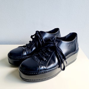 Puede incluir: Par de zapatillas de plataforma de cuero negro con cierre de cordones.