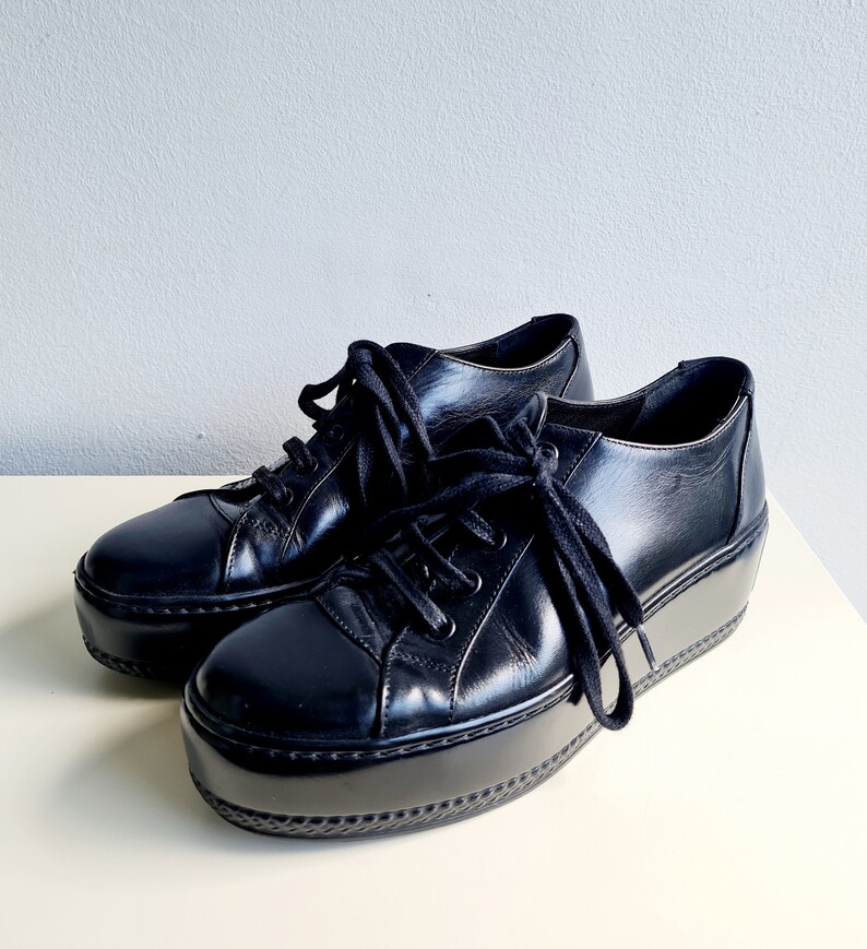 Puede incluir: Par de zapatillas de plataforma de cuero negro con cierre de cordones.