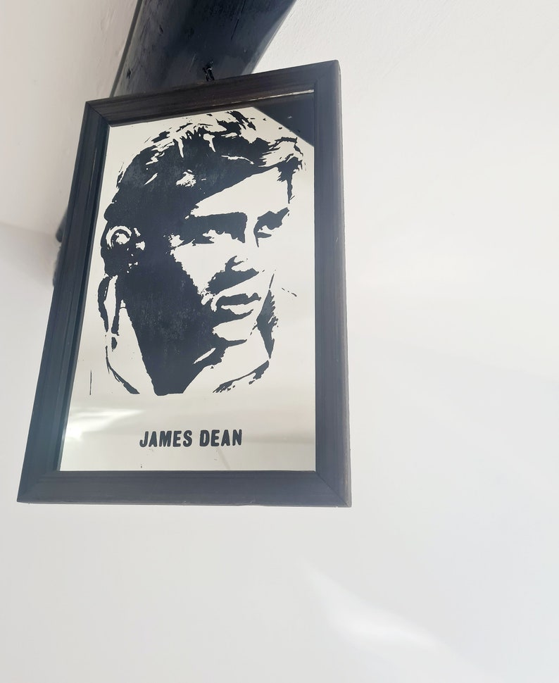 May include: A black and white framed mirror with a silhouette of James Dean's face and the text "JAMES DEAN" printed below the image.