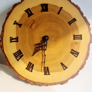 May include: A wooden clock with Roman numeral markings on a natural wood slice. The clock hands are black metal.