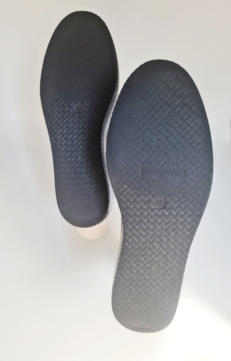 Puede incluir: Primer plano de las suelas negras de dos pares de zapatos. Las suelas tienen un patr&oacute;n texturizado y el tama&ntilde;o 39 est&aacute; impreso en la parte inferior.