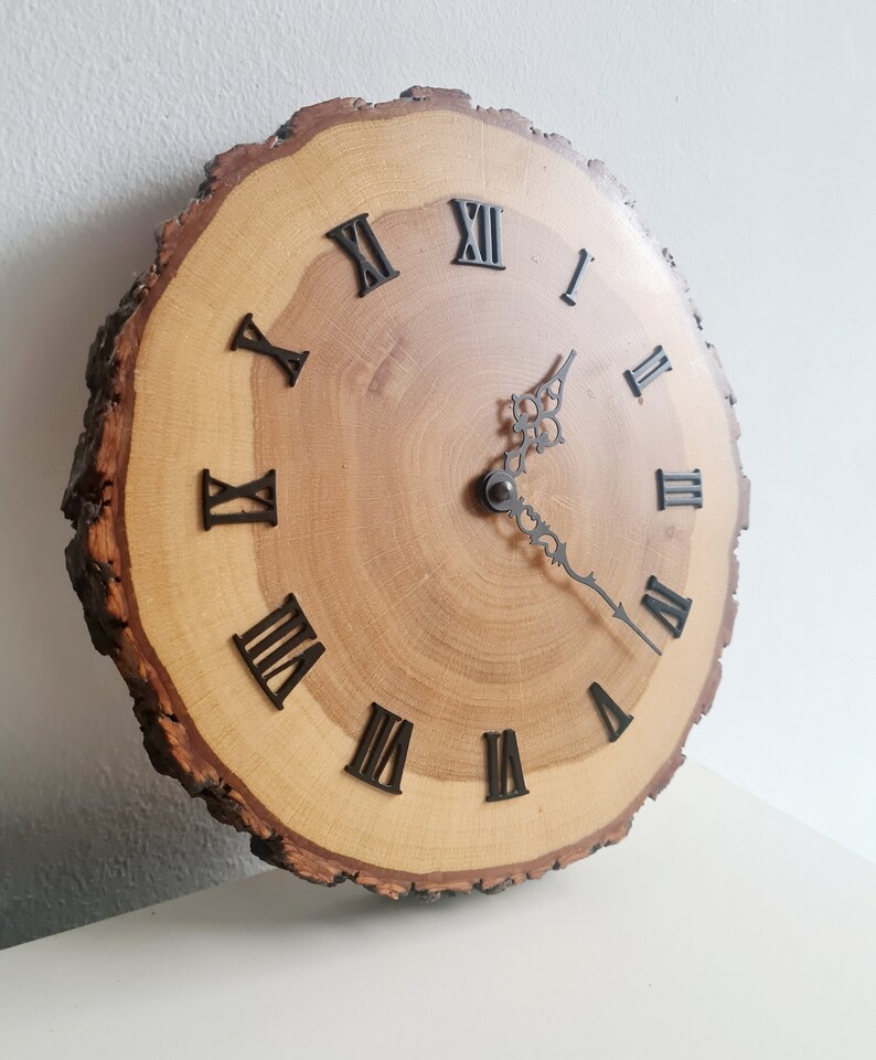 May include: A wooden clock with Roman numeral markings on a natural wood slice. The clock face is made of wood with a natural grain pattern. The clock hands are black metal.