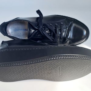Puede incluir: Zapatillas de plataforma de cuero negro con suela gruesa de goma y cierre de cordones. La suela tiene un patr&oacute;n texturizado y las palabras "made in Italy" est&aacute;n impresas en la parte inferior.