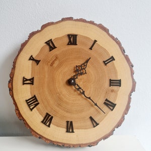 May include: A wooden clock with Roman numeral markings on a natural wood slice. The clock hands are black metal.