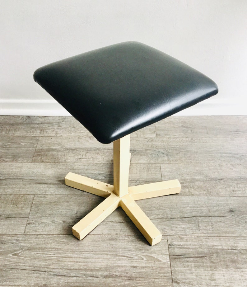 May include: A black upholstered square stool with a cream-coloured, five-pointed star base.