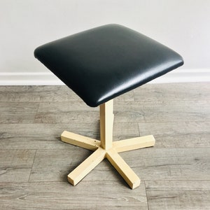 May include: A black upholstered square stool with a cream-coloured, five-pointed star base.