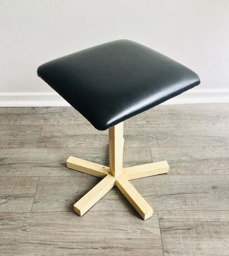 May include: A black upholstered square stool with a cream-coloured, five-pointed star base.