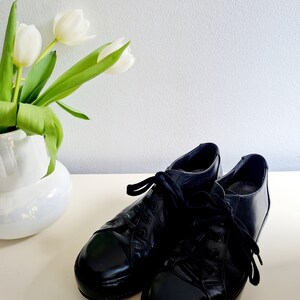 Puede incluir: Un par de zapatos negros de cuero con cordones y acabado brillante. Los zapatos tienen una punta redonda y una suela gruesa.