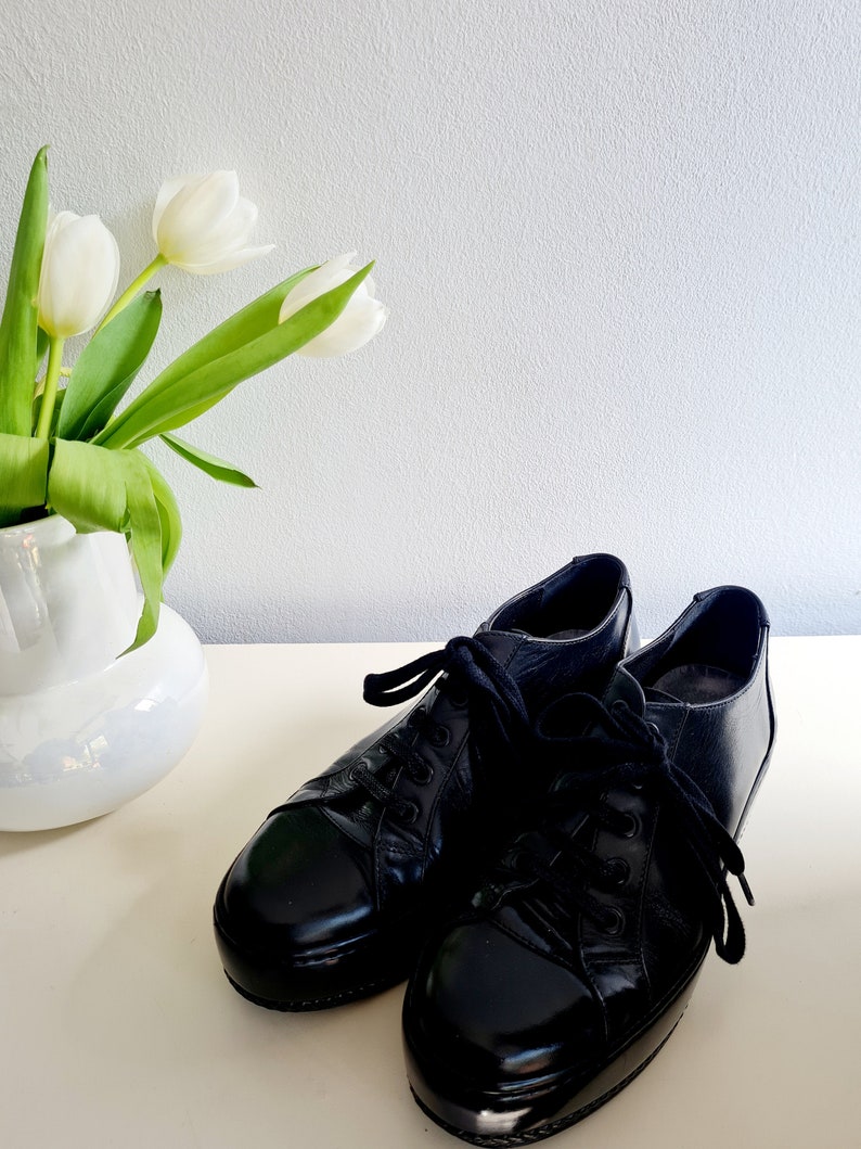 Puede incluir: Un par de zapatos negros de cuero con cordones y acabado brillante. Los zapatos tienen una punta redonda y una suela gruesa.