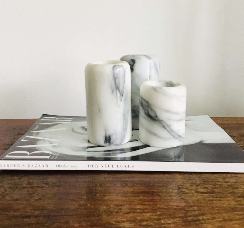 May include: Three white marble candle holders with gray veining. The candle holders are arranged in a row on a magazine.