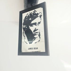 May include: Black and white silhouette of James Dean in a framed mirror. The mirror has a black frame and the text "JAMES DEAN" is printed below the image.