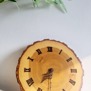 May include: A wooden clock with Roman numeral markings on a natural wood slice. The clock hands are black metal.