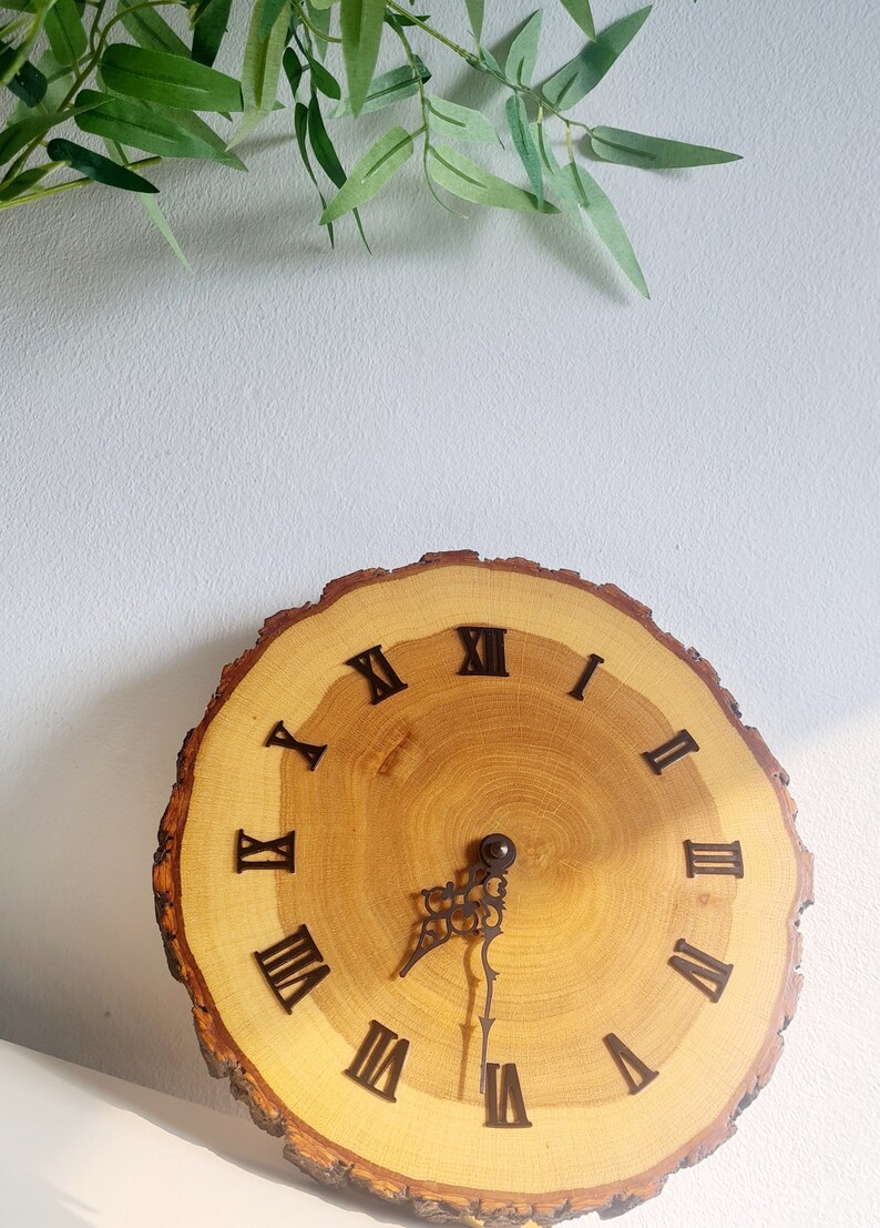 May include: A wooden clock with Roman numeral markings on a natural wood slice. The clock hands are black metal.
