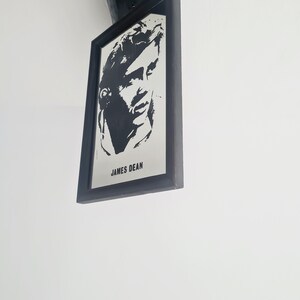 May include: Black and white framed print of James Dean, a famous actor. The print is in a black frame and is hanging on a white wall.