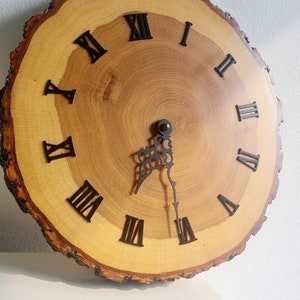 May include: A wooden clock with Roman numeral markings on a natural wood slice. The clock face is light brown with dark brown wood grain. The clock hands are black.