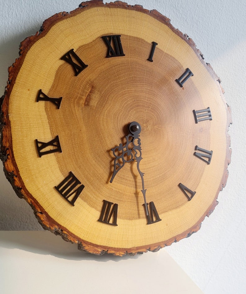 May include: A wooden clock with Roman numeral markings on a natural wood slice. The clock face is light brown with dark brown wood grain. The clock hands are black.
