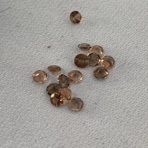 May include: A group of small, round, brown gemstones. The gemstones are scattered on a white fabric surface.