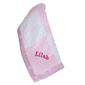 May include: A pink and white checkered baby blanket with a satin border. The blanket is personalized with the name "Lilah" embroidered in pink.