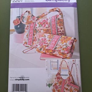 May include: Simplicity sewing pattern 2201 featuring a floral print handbag and matching clutch. The pattern includes instructions for creating a tote bag, a shoulder bag, and a wallet. The pattern's text includes "ONE SIZE" and "simplicity.com".