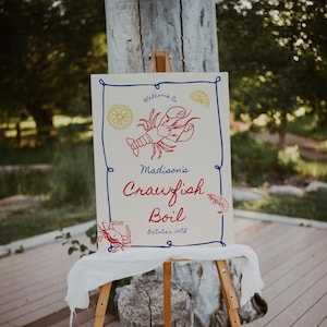 May include: A white sign with blue and red lettering announces "Welcome to Madison's Crawfish Boil, October 27th". The sign features a red crawfish illustration, a lemon, and a crab.