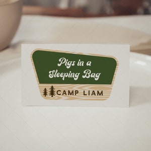 May include: A green and brown sign with the text "Pigs in a Sleeping Bag" and "Camp Liam" in white lettering.