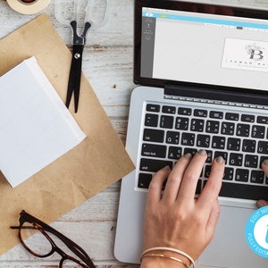 May include: A person is using a laptop to edit a logo design. The logo is for "Sarah Baker, a handcrafted blog". The laptop screen shows a design template with a floral motif and the text "EDIT WITH Templett FULLY EDITABLE TEMPLATE".