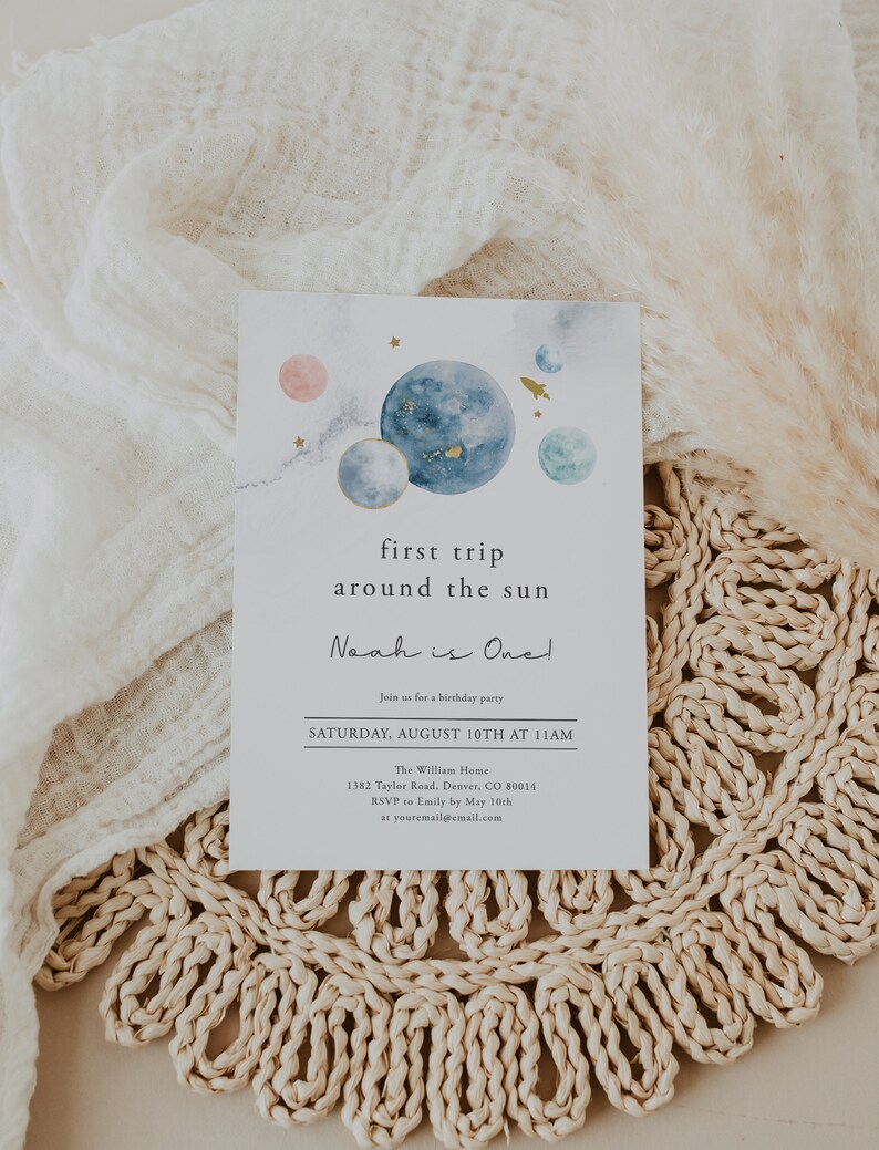 May include: A watercolour-style invitation for a first birthday party with a space theme. The invitation features planets, stars, and a rocket ship. The text reads "first trip around the sun Noah is One!"  Join us for a birthday party Saturday, August 10th at 11 AM. The William Home 1382 Taylor Road, Denver, CO 80014 RSVP to Emily by 10th May at youremail@email.com