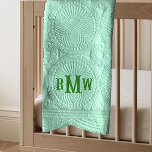 May include: A light green baby blanket with a quilted pattern of circles and a monogram of the letters "RMW" in green embroidery.