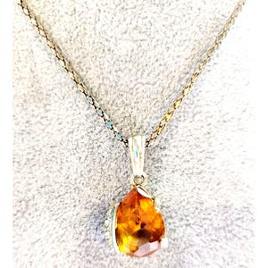 May include: A silver necklace with a teardrop-shaped pendant. The pendant is a faceted, amber-colored gemstone with a silver setting. The chain is a delicate, linked design.
