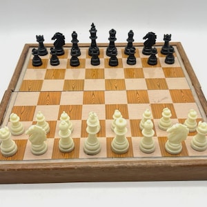 Puede incluir: Un juego de ajedrez de madera con piezas negras y blanquecinas dispuestas sobre un tablero a cuadros. El tablero está dentro de un marco de madera. Las piezas están en sus posiciones iniciales, listas para una partida de ajedrez.