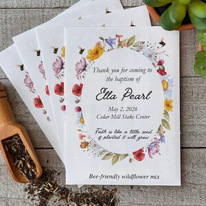May include: White seed packets with floral designs and the text "Thank you for coming to the baptism of Ella Pearl." The packets are labeled "Bee-friendly wildflower mix."