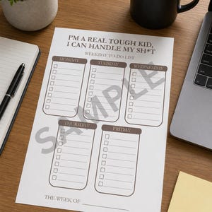 Peut inclure: Une feuille de liste de tâches blanche avec le texte "I'M A REAL TOUGH KID, I CAN HANDLE MY SH*T". La feuille est divisée en cinq sections pour chaque jour de la semaine, avec des cases à cocher pour les tâches. Un stylo noir, un carnet et une tasse à café sont également visibles.