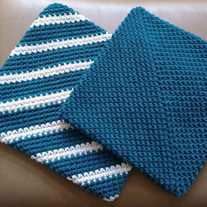 May include: Two handmade, square crochet potholders. One is solid teal, the other has diagonal white stripes on a teal background. The potholders are made of thick yarn and are likely heat-resistant.