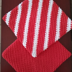 May include: Two red crocheted pot holders, one with white stripes. The striped pot holder is on top of the solid red pot holder.