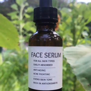 Op de afbeelding: Een bruine glazen fles met een zwarte druppelaar en een wit etiket met de tekst "FACE SERUM" en de voordelen: "VOOR ALLE HUIDTYPES GEMAKKELIJK OPGENOMEN ANTI-VEROUDERING ACNE BESTRIJDING VERZACHT DE HUIDTOON RIJKE AANTAL ANTIOXIDANTEN".