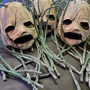 Peut inclure: Trois visages blancs effrayants, ressemblant &agrave; des masques, avec des cheveux verts et filandreux. Les masques ont une bouche cousue et des yeux avec des pupilles noires.