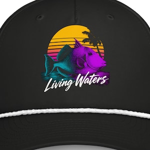 May include: A black baseball cap featuring a white rope detail across the brim. The front displays a graphic of a purple and blue fish swimming in front of a yellow sunset and palm tree silhouette, with the white script text Living Waters.
