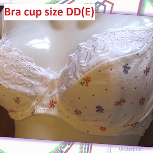 May include: A white bra with floral patterns and lace detailing. The bra features a delicate design with small, colourful flowers scattered across the fabric. The text "Bra cup size DD(E)" is visible at the top.