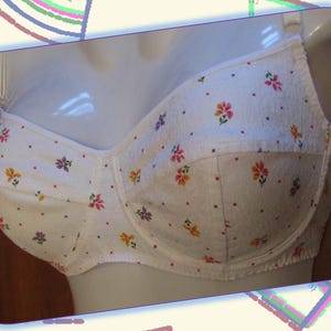 Puede incluir: Sujetador de algodón blanco con estampado floral. El sujetador tiene una copa acolchada y tirantes ajustables.