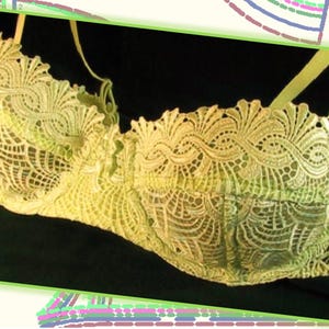 Puede incluir: Un sujetador de encaje delicado de color crema con un patrón floral. El sujetador tiene tirantes ajustables y un cierre de gancho y ojo en la espalda.