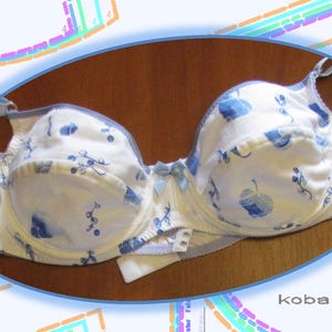 Puede incluir: Sujetador blanco con estampado floral azul. El sujetador tiene tirantes ajustables y cierre de gancho y ojo en la espalda.