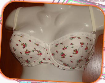 May include: White bra with a floral pattern of red and green flowers. The bra has adjustable straps and a lace trim along the top edge. The bra is displayed on a mannequin.