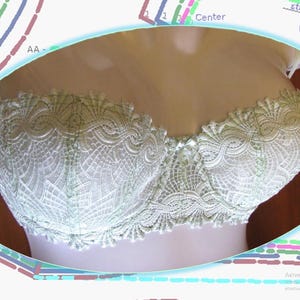 Puede incluir: Un sujetador de encaje verde claro con un delicado patrón floral. El sujetador está en un maniquí de busto blanco.