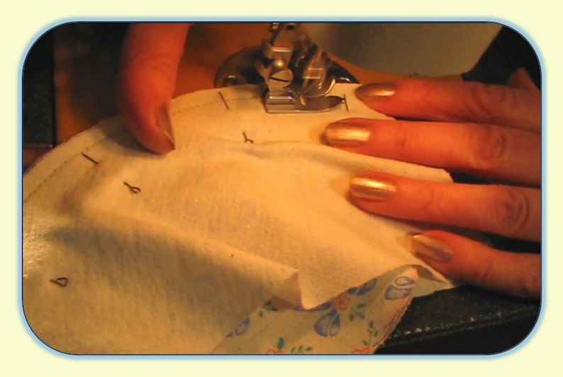 May include: Close-up of a sewing machine needle going through a piece of white fabric. The fabric has markings on it, and the person's fingers are visible on the fabric.