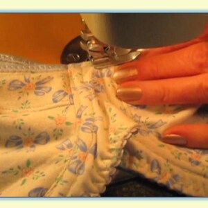 May include: A close-up of a sewing machine needle going through a piece of fabric with a floral pattern. The fabric is being held in place by a hand.