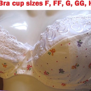 May include: A white bra featuring a floral pattern with small red, orange, and purple flowers and dots. The upper cup section has white embroidered floral detailing and a small center bow. The text Bra cup sizes F, FF, G, GG, H is visible.