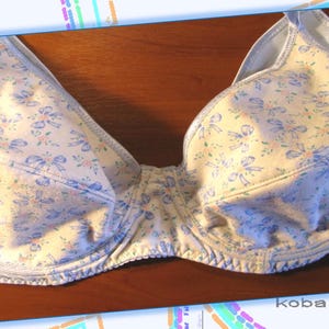 May include: A white bra with a blue floral pattern and a light blue trim. The bra has a delicate bow design throughout the fabric.