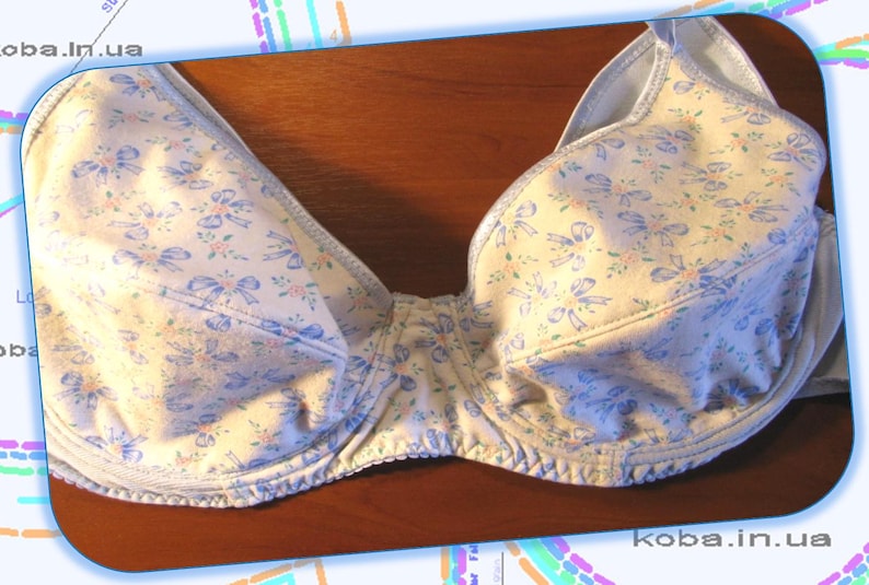 May include: A white bra with a blue floral pattern and a light blue trim. The bra has a delicate bow design throughout the fabric.